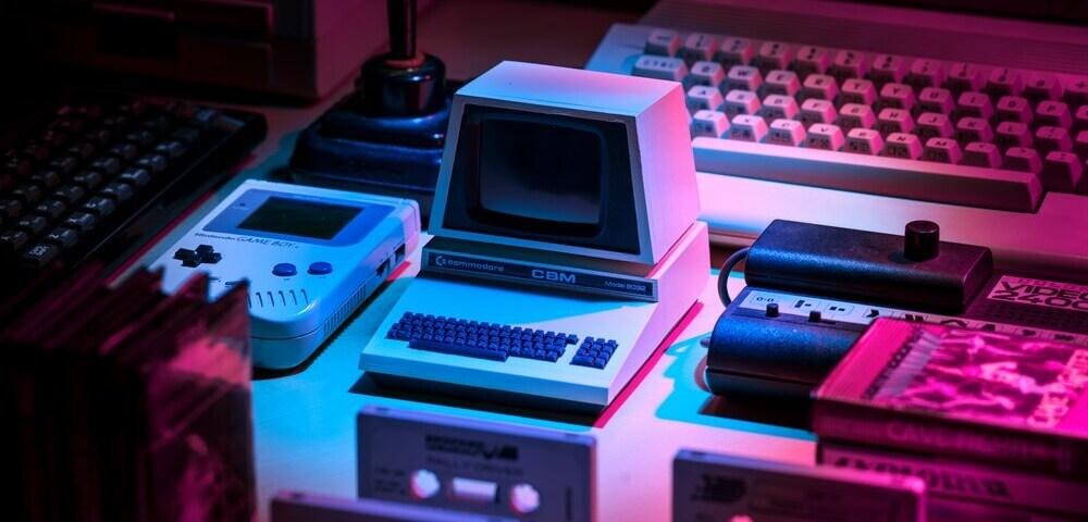 Retro computers and cassette tapes on a table under pink an blue light